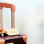 Suitcase with TRAVEL INSURANCE label on light blurred background