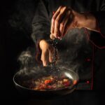 Cooking fresh vegetables. The chef adds salt to a steaming hot pan. Grande cuisine idea for a hotel with advertising space